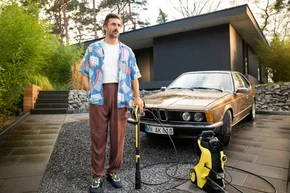 Person mit Hochdruckreiniger vor Auto